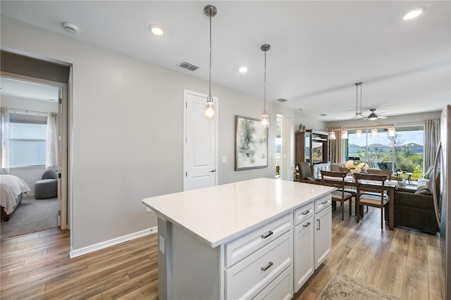 kitchen with wood-type flooring, hanging light fixtures, white cabinets, and a kitchen island