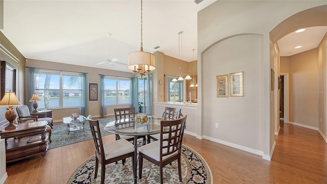 dining area featuring hardwood / wood-style floors, ceiling fan with notable chandelier, and high vaulted ceiling