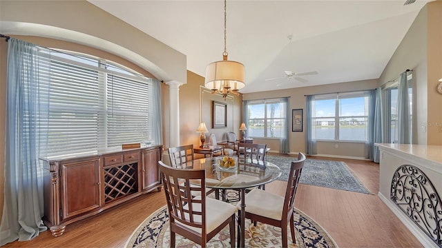 dining space featuring ceiling fan with notable chandelier, light wood-type flooring, vaulted ceiling, and ornate columns