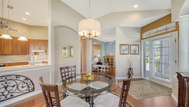 dining room with ornate columns, ceiling fan with notable chandelier, sink, high vaulted ceiling, and light hardwood / wood-style flooring