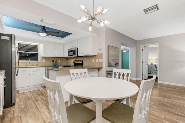 dining room with a tray ceiling, sink, a chandelier, and light hardwood / wood-style flooring