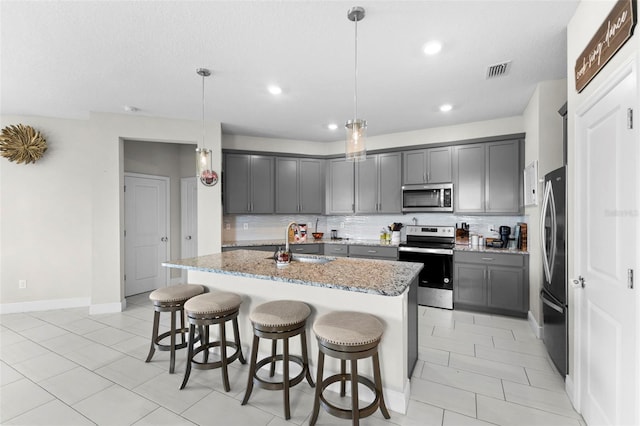 kitchen with light stone counters, pendant lighting, tasteful backsplash, a center island with sink, and stainless steel appliances