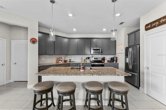 kitchen featuring dark stone counters, hanging light fixtures, a kitchen island with sink, and stainless steel appliances