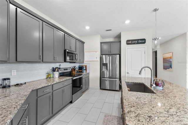 kitchen featuring gray cabinetry, decorative light fixtures, sink, stainless steel appliances, and light stone countertops