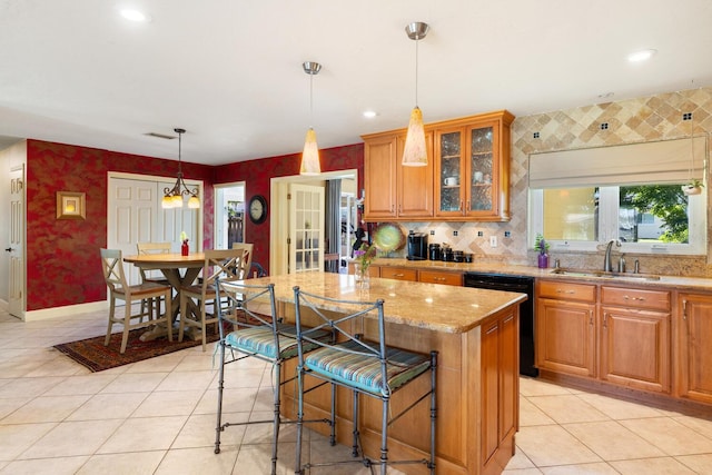 kitchen featuring light stone counters, sink, dishwasher, a kitchen breakfast bar, and a center island