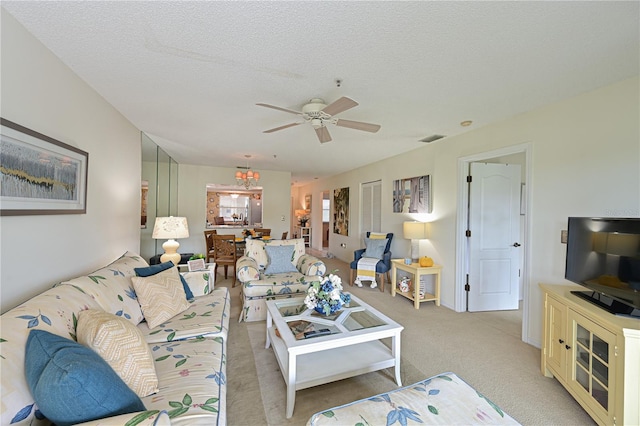 living area featuring a textured ceiling, a ceiling fan, visible vents, and light colored carpet