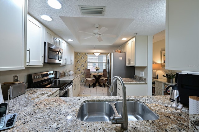 kitchen with a textured ceiling, a sink, visible vents, appliances with stainless steel finishes, and a tray ceiling