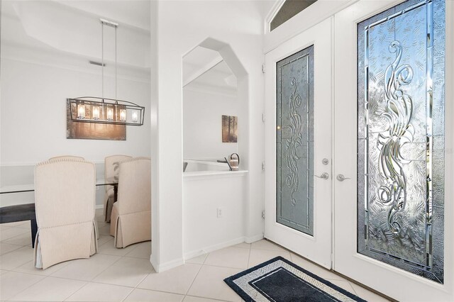 tiled entryway featuring an inviting chandelier, crown molding, and french doors