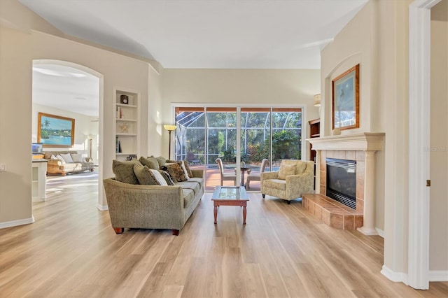 living room with light hardwood / wood-style floors, built in features, and a tiled fireplace