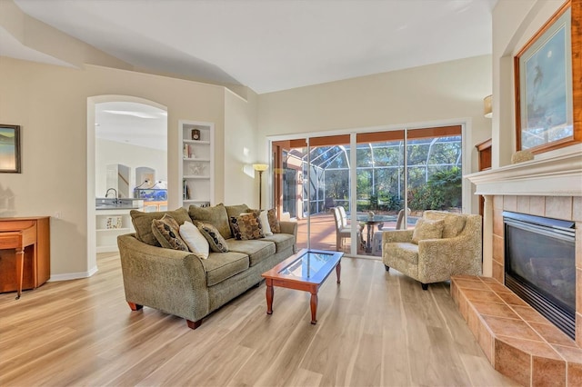 living room with a tiled fireplace, built in features, and light wood-type flooring