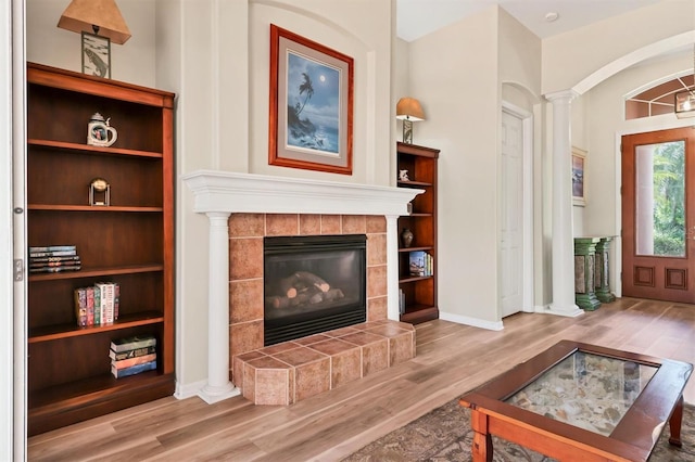 living area with decorative columns, a tile fireplace, and hardwood / wood-style flooring