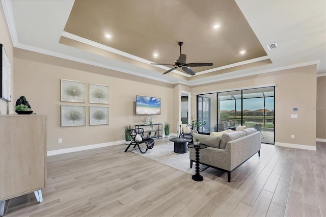 living room with a raised ceiling, ceiling fan, light hardwood / wood-style flooring, and ornamental molding