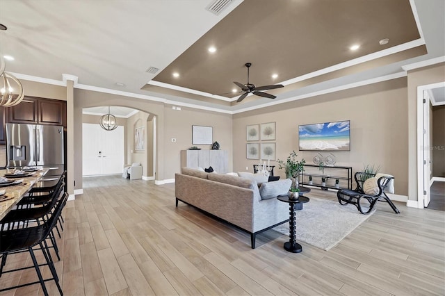 living room with ceiling fan with notable chandelier, light hardwood / wood-style floors, a raised ceiling, and ornamental molding