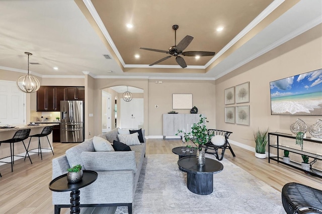 living room with ceiling fan with notable chandelier, light hardwood / wood-style flooring, a raised ceiling, and ornamental molding