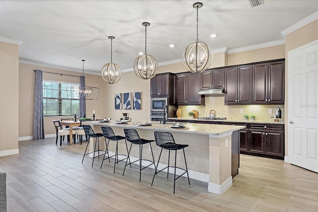 kitchen with a breakfast bar, dark brown cabinetry, built in microwave, a kitchen island with sink, and hanging light fixtures