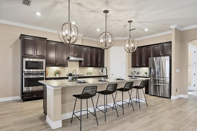 kitchen featuring a center island with sink, pendant lighting, light stone countertops, and appliances with stainless steel finishes