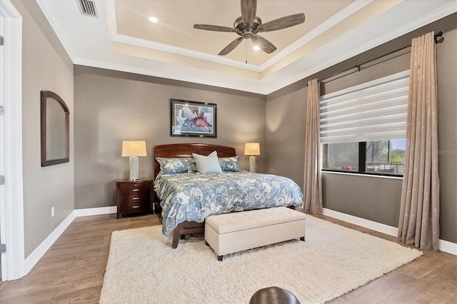 bedroom with a tray ceiling, ceiling fan, crown molding, and wood-type flooring