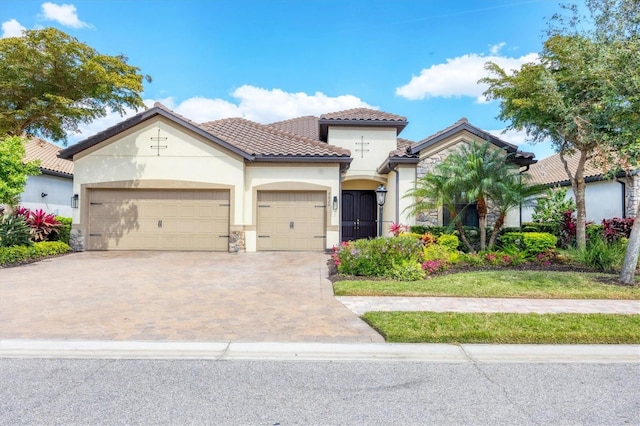 mediterranean / spanish home with a garage, decorative driveway, a tile roof, and stucco siding