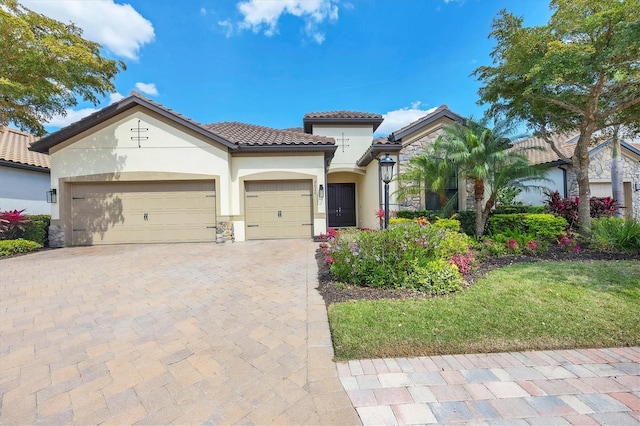 mediterranean / spanish home featuring decorative driveway, stucco siding, an attached garage, stone siding, and a tiled roof