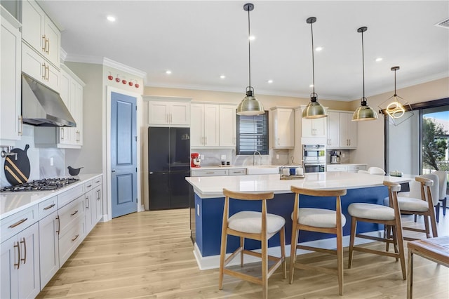 kitchen featuring appliances with stainless steel finishes, a kitchen breakfast bar, a kitchen island with sink, light hardwood / wood-style flooring, and pendant lighting