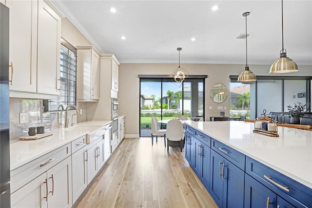 kitchen featuring hanging light fixtures, ornamental molding, blue cabinetry, white cabinets, and light hardwood / wood-style floors