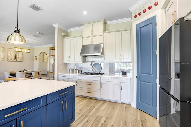 kitchen featuring ornamental molding, pendant lighting, blue cabinets, light hardwood / wood-style floors, and tasteful backsplash