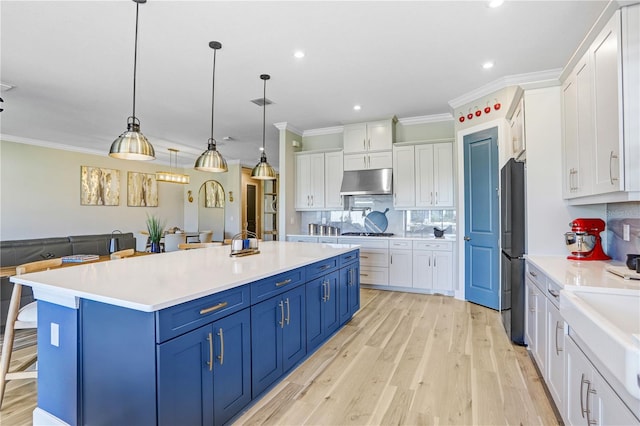 kitchen with appliances with stainless steel finishes, light wood-type flooring, blue cabinets, hanging light fixtures, and white cabinetry