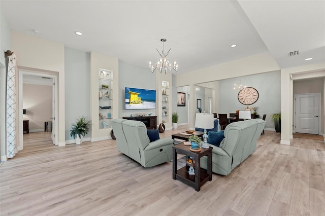 living room with built in shelves, light hardwood / wood-style flooring, a fireplace, and a chandelier