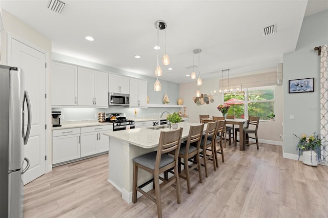 kitchen with pendant lighting, a kitchen island with sink, light hardwood / wood-style flooring, white cabinetry, and appliances with stainless steel finishes