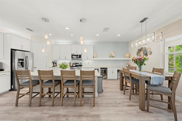 kitchen with pendant lighting, light wood-type flooring, a center island, white cabinetry, and stainless steel appliances