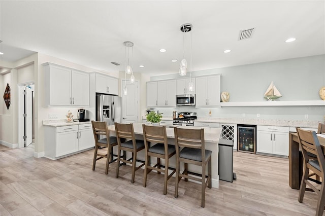 kitchen featuring hanging light fixtures, wine cooler, stainless steel appliances, a center island, and light hardwood / wood-style flooring