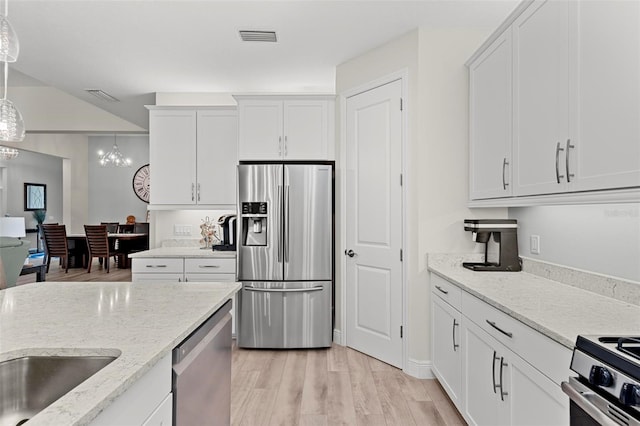 kitchen featuring light wood-type flooring, stainless steel appliances, hanging light fixtures, and white cabinetry