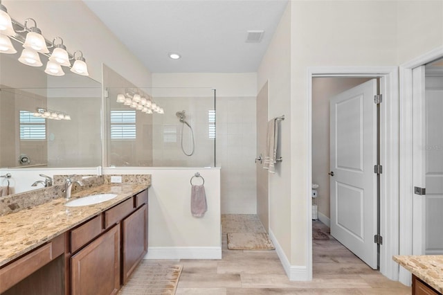 bathroom featuring a tile shower, vanity, and wood-type flooring