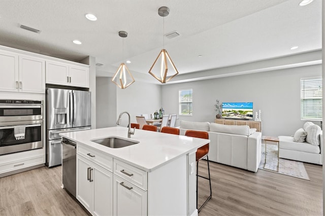 kitchen with plenty of natural light, a kitchen island with sink, sink, and white cabinets