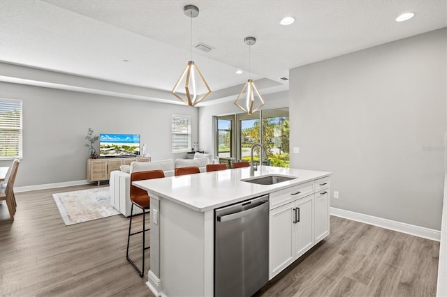 kitchen with a kitchen island with sink, stainless steel dishwasher, white cabinets, sink, and hanging light fixtures