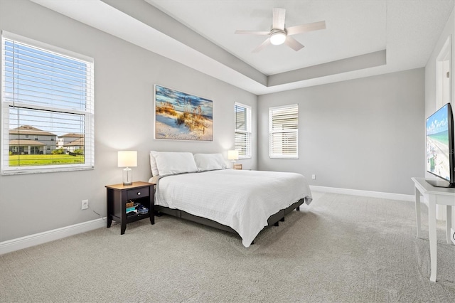 carpeted bedroom featuring multiple windows, ceiling fan, and a tray ceiling