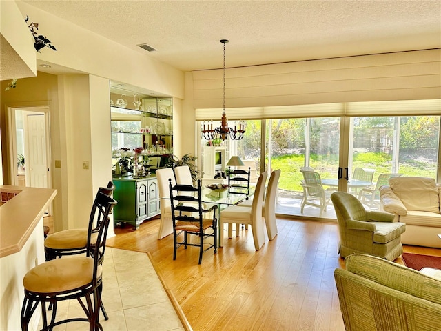 dining room with an inviting chandelier, a textured ceiling, and light wood-type flooring