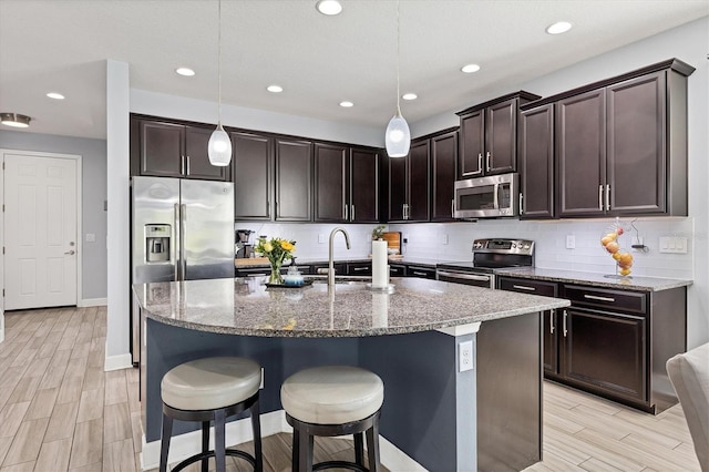 kitchen with pendant lighting, sink, a kitchen island with sink, appliances with stainless steel finishes, and light wood-type flooring