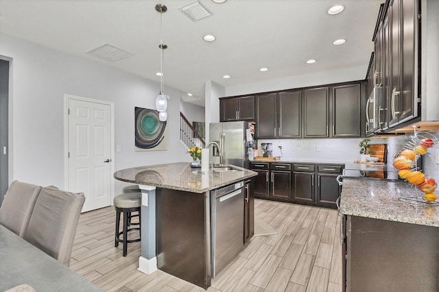 kitchen featuring light stone counters, an island with sink, hanging light fixtures, sink, and stainless steel appliances