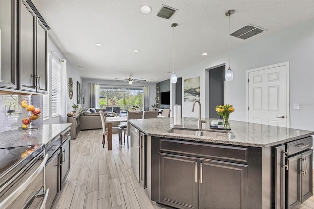 kitchen with pendant lighting, a kitchen island with sink, sink, light stone countertops, and ceiling fan