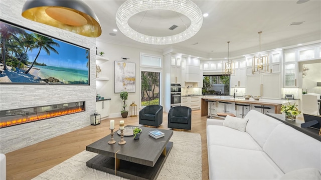 living room featuring light wood-type flooring, sink, a fireplace, crown molding, and a wealth of natural light