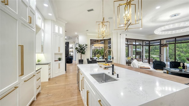 kitchen with pendant lighting, light wood-type flooring, sink, white cabinetry, and ornamental molding