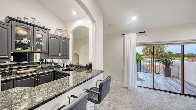 kitchen featuring light carpet, sink, vaulted ceiling, and dark stone countertops