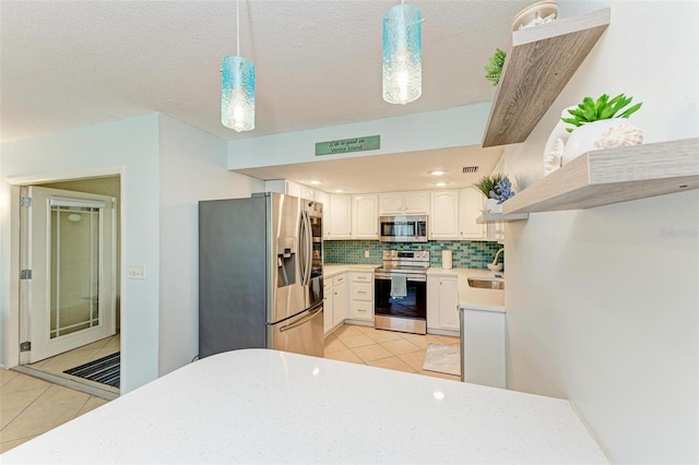 kitchen featuring appliances with stainless steel finishes, white cabinets, backsplash, decorative light fixtures, and sink