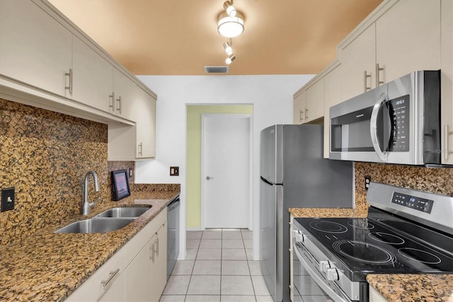 kitchen with sink, appliances with stainless steel finishes, dark stone countertops, backsplash, and light tile patterned flooring