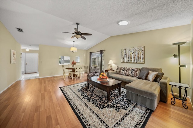 living room featuring lofted ceiling, light hardwood / wood-style flooring, a textured ceiling, and ceiling fan