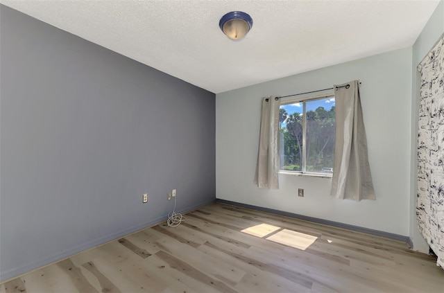 spare room featuring a textured ceiling and light hardwood / wood-style floors