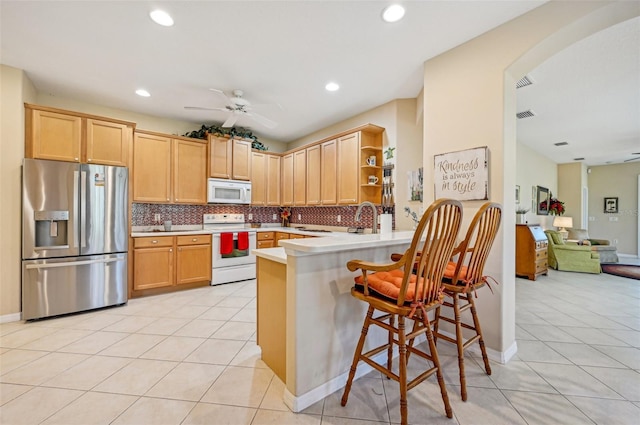 kitchen featuring a kitchen breakfast bar, light brown cabinetry, kitchen peninsula, and white appliances