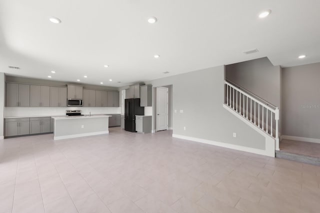 kitchen with a center island with sink, appliances with stainless steel finishes, light tile patterned flooring, and gray cabinets