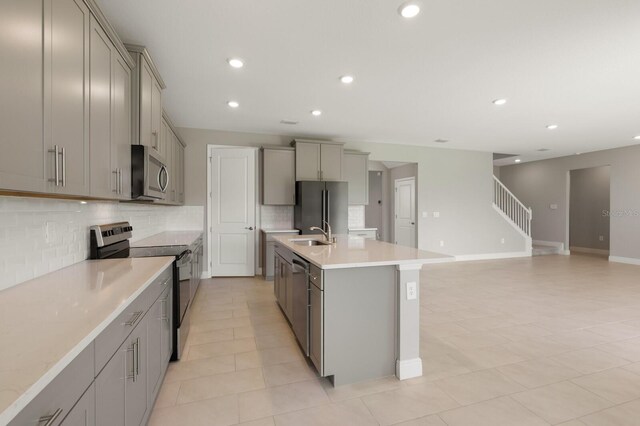 kitchen featuring appliances with stainless steel finishes, gray cabinetry, a center island with sink, and backsplash